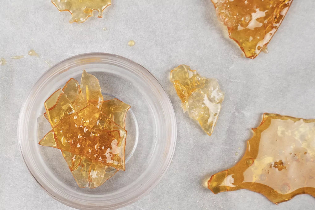 A top down view of amber colored CBD shatter strewn across a white surface.
