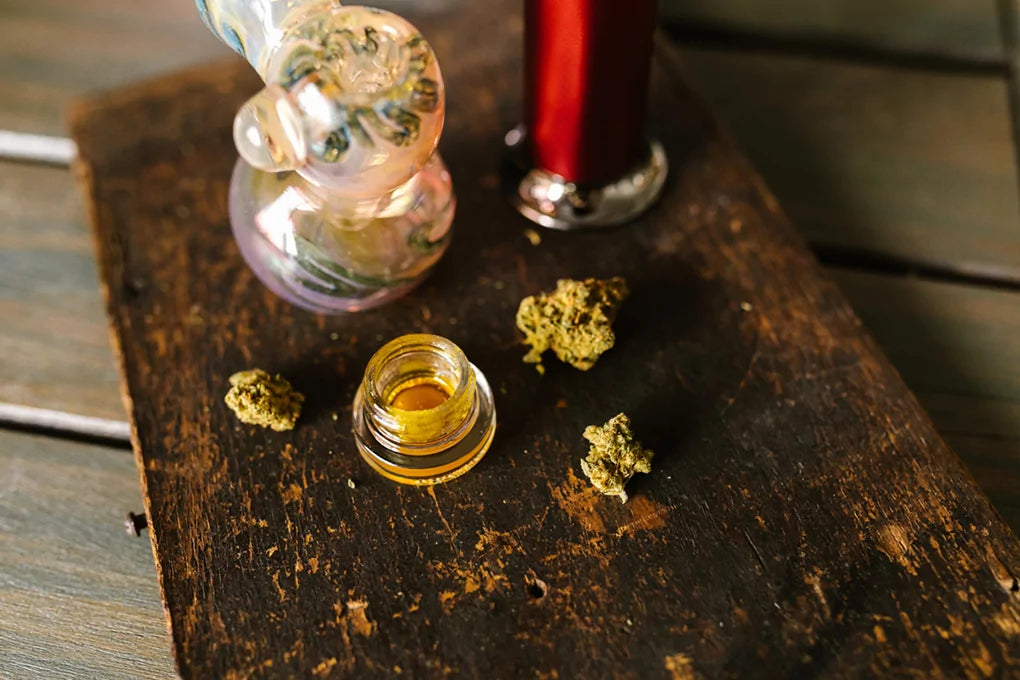 A dab rig and all its accessories, including a little jar of amber dab weed sit on a table.