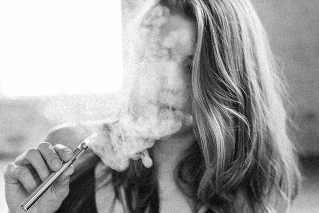 A woman blows out smoke after inhaling an HHC cart from a vape pen.