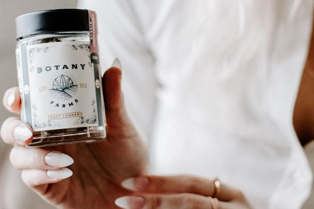 A close up shot of a person holding a Botany Farms branded jar of gummies.