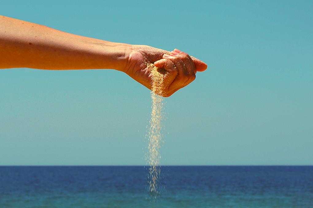 Sand slipping through clenched fist, against blue sky and serene sea
