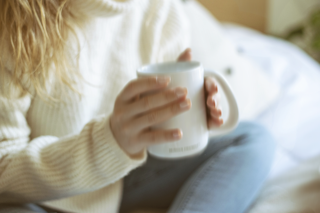 Woman in white sweater and blue jeans holding a white cup