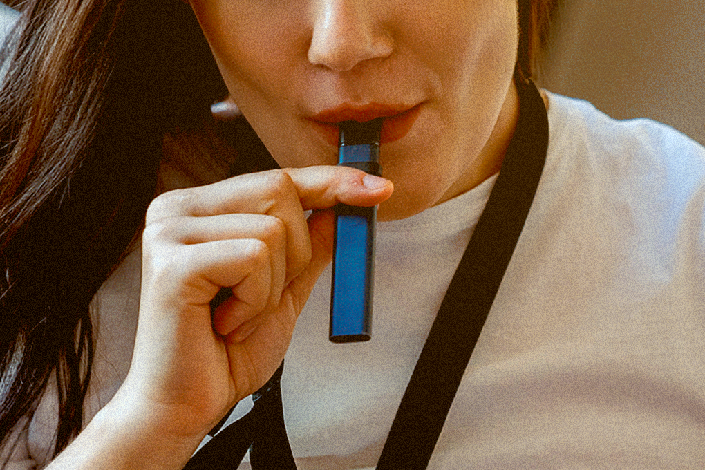A woman with a slight smile, holding a vape cartridge in her lips