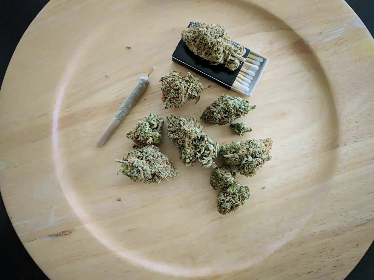 Some buds of high CBD low THC cannabis on a wooden plate with some matches and a joint