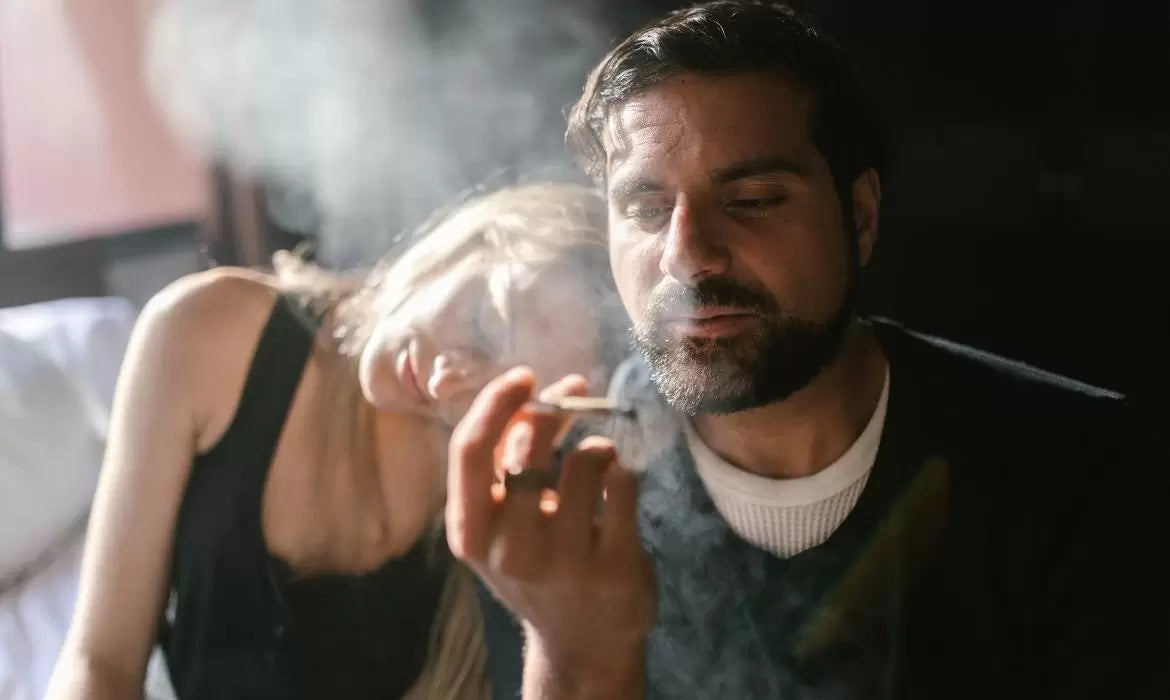 Man and woman smoke a joint while sitting in bed.
