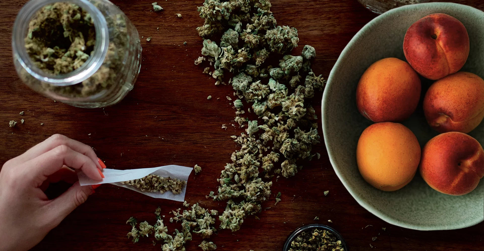 A pile of peach fuzz cannabis strain with a joint being rolled next to a bowl of peaches