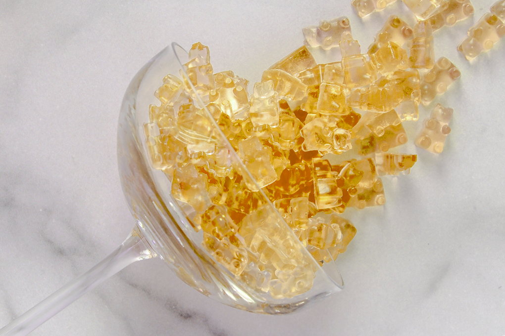 Champagne Gummy Bears arranged on a glass, with champagne being poured into it against a clean white background