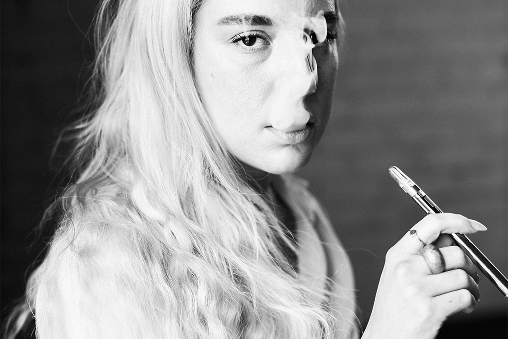 A woman stares intensely into the camera as she blows out smoke from her terpene vape