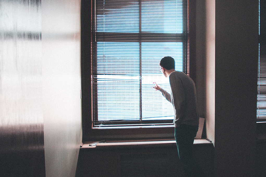A man looks through a window in a paranoid fashion.